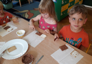 Dzieci smarują herbatniki serkiem czekoladowym.