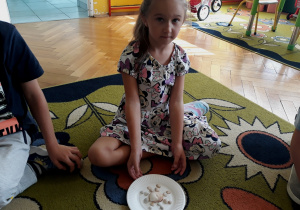 Dziewczynka pokazuje kompozycję z muszli na talerzyku.
