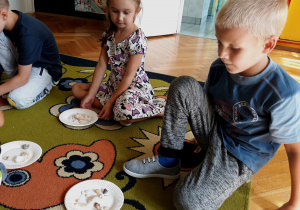 Dzieci pokazują ułożone kompozycje z muszli na talerzykach.
