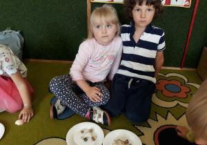 Dzieci pokazują ułożone kompozycje z muszli na talerzykach.
