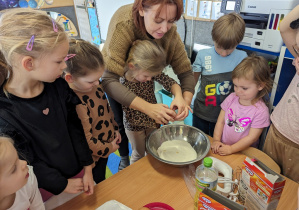 Dziewczynka rozbija jajko z pomocą nauczycielki.