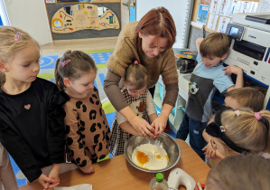 Dziewczynka rozbija jajko z pomocą nauczycielki.