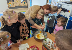 Dziewczynka rozbija jajko z pomocą nauczycielki.