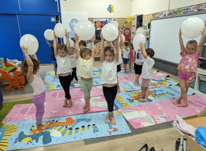 Dzieci wykonują ćwiczenia z balonami uniesionymi nad głowami.