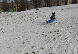 Chłopiec zjeżdża z górki na sankach.