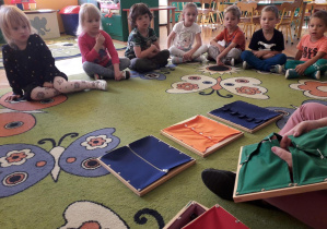 Dzieci siedzą na dywanie, na którym leżą różne typy zapięć.