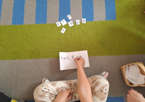 Dziewczynka uzupełnia literą wyraz.