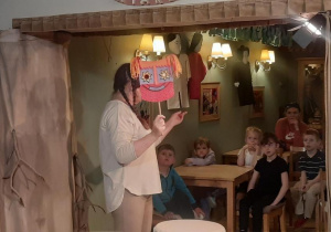 Aktorka prezentuje dzieciom o rodzajach maskę teatralną.