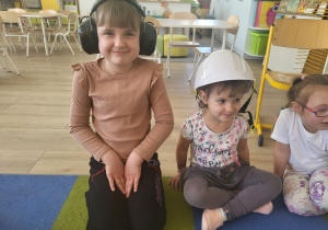 Dziewczynki przymierzają słuchawki wyciszające i kask ochronny.