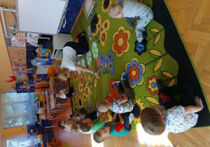 Nauczycielka rozkłada szablony owoców na dywanie.