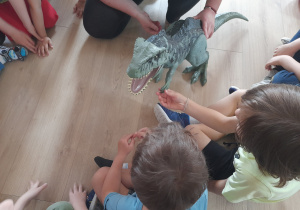 Dzieci dotykają plastikowego dinozaura.