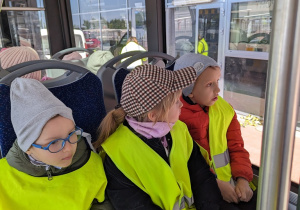 Dzieci jadą autobusem lotniskowym po terenie portu lotniczego.