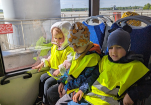 Dzieci jadą autobusem lotniskowym po terenie portu lotniczego.