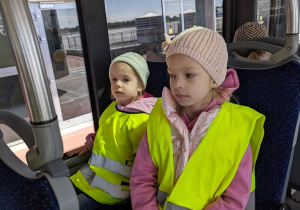 Dzieci jadą autobusem lotniskowym po terenie portu lotniczego.