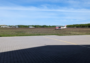 Mały samolot ląduje na pasie przy hangarze.