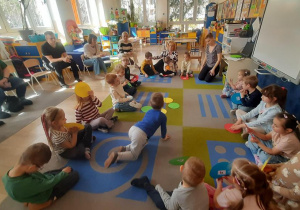 Dzieci siedzą na dywanie, trzymając w dłoni kolorowe kółko z sylabą.