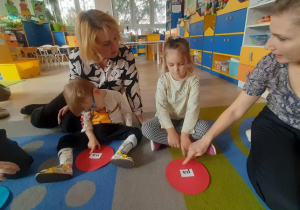 Dziewczynka z pomocą nauczycielki odczytuje sylabę na swoim kółku.
