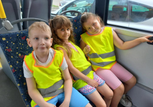 Dzieci jadą autobusem, ubrane w kamizelki odblaskowe.