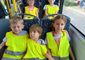 Dzieci jadą autobusem, ubrane w kamizelki odblaskowe.