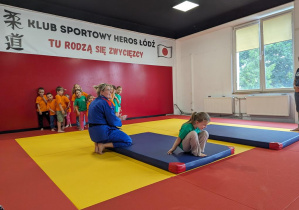 Dzieci wykonują przewrót w przód na materacu pod okiem trenera.