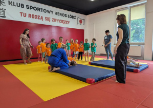 Dzieci wykonują przewrót w przód na materacu pod okiem trenera.