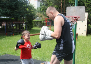 Chłopiec w rękawicach boksuje z trenerem.