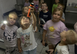 Dzieci zwiedzają przedszkole z latarkami.