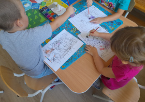 Dzieci malują farbami siedząc przy stoliku.