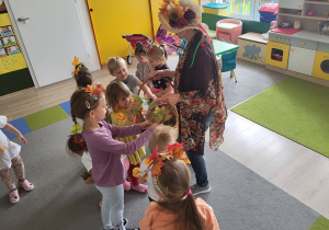 Nauczycielka przebrana za jesień, dzieci zbierają liście.