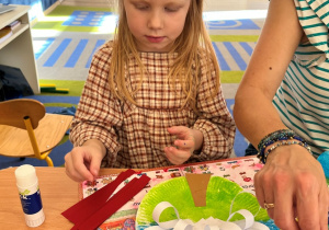 Dziewczynka skleja paski czerwonego paieru.