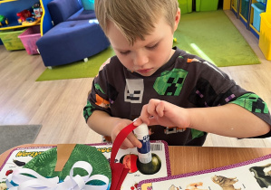 Chłopiec smaruje klejem pasek czerwonego papieru.