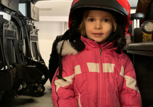 Dziewczynka pozuje w kasku strażackim.