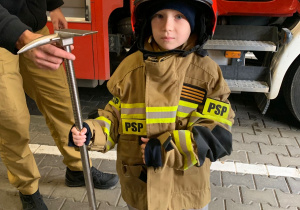 Dziecko pozuje do zdjęcia w stroju strażaka.