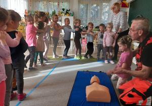 Dzieci stoją i słuchają ratownika medycznego.