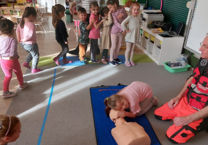 Dziewczynka ćwiczy na fantomie pod kierunkiem ratownika medycznego.