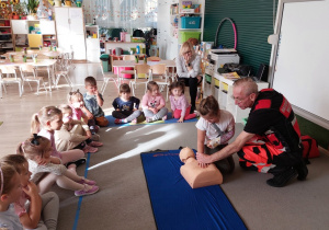 Dziecko ćwiczy na fantomie pod kierunkiem ratownika medycznego.