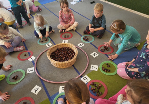 Dzieci siedzą, bawią się w grę z cyframi i kasztanami.