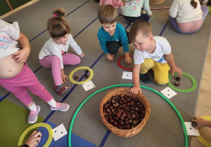 Dzieci bawią się w grę z liczbami i kasztanami.