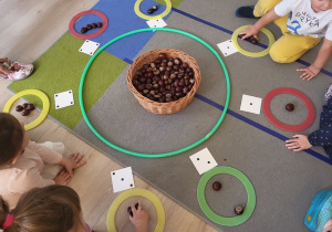 Dzieci siedzą, bawią się w grę z kasztanami.