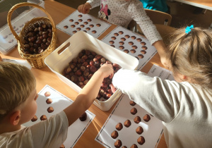 Dzieci układają z kasztanów wzory.