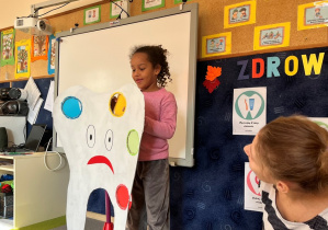 Dziewczynka zakleja dziurę zęba żółtym kółkiem.