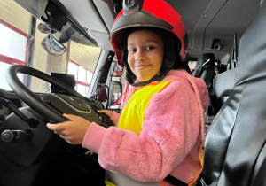 Dziecko w kasku, w wozie strażackim.