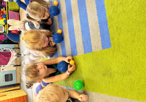 Dzieci leżna na brzuchu na dywanie z piłeczkami - wieksza i mniejszą.