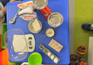 Na stoliku waga szalkowa i elektroniczna i bagażowa do zajęć, akcesoria do ważenia.