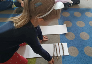 Dziecko układa na białej kartce patyki od najmniejszego do największego.