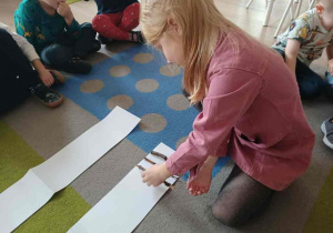 Dziecko układa na białej kartce patyki od najmniejszego do największego.