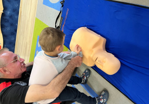 Dziecko z ratownikiem układa dłonie na fantomie w okolicy mostka.