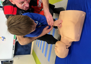 Dziecko z ratownikiem układa dłonie na fantomie.