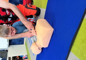 Dziecko z ratownikiem układa dłonie na fantomie.