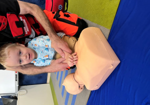 Dziecko z ratownikiem układa dłonie na fantomie.